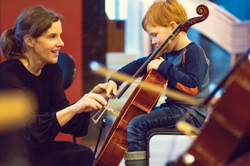 Et barn prøver en cello med hjelp fra en musiker