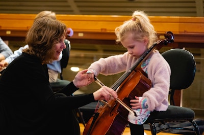 A child playing the cello, assisted by a musician from the Oslo Philharmonic