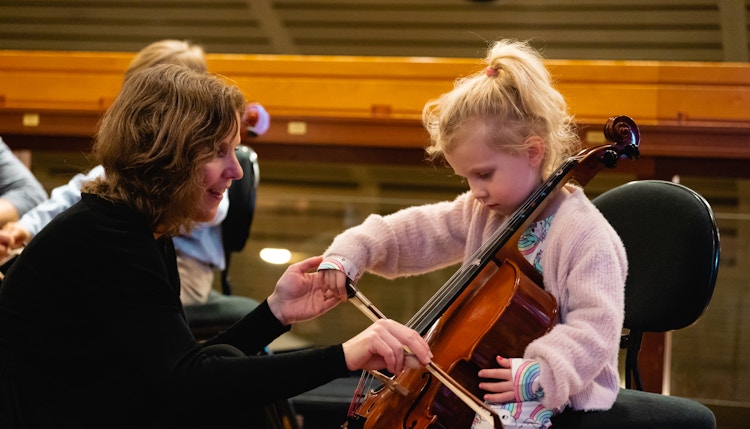 A child playing the cello, assisted by a musician from the Oslo Philharmonic